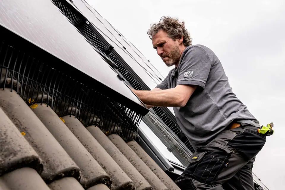 Plaatser klemt een BirdBlocker profiel onder zonnepanelen op een pannendak