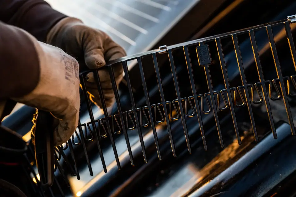 Hand met werkhandschoen bevestigt de RVS klem van BirdBlocker aan het paneelframe