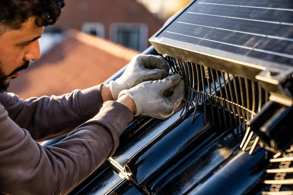 Plaatser bevestigt BirdBlocker onder een zonnepaneel met handschoenen